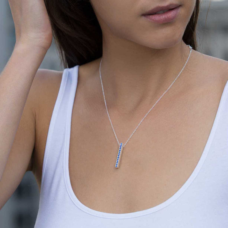 A brunette woman wears a blue sapphire and sterling silver pendant necklace